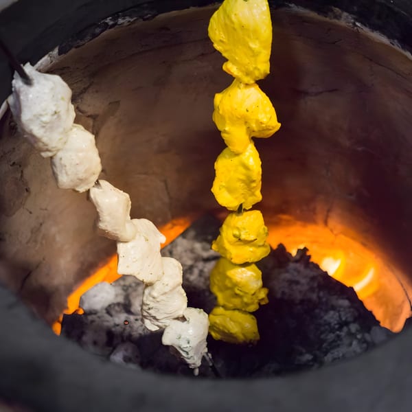 Marinated chicken skewers, white and yellow, cooking inside a fiery tandoor oven at Mint Masala.
