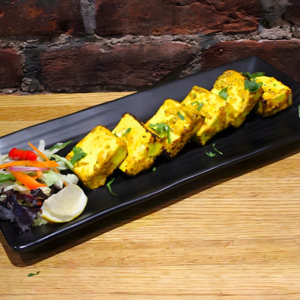 Mint Masala's paneer tikka, golden-brown cheese cubes with cilantro, served with a side salad and lemon.