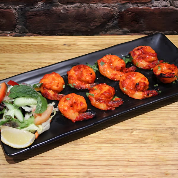 Mint Masala's Indian Tandoori Prawns, bright red and garnished with herbs, served with a side salad.