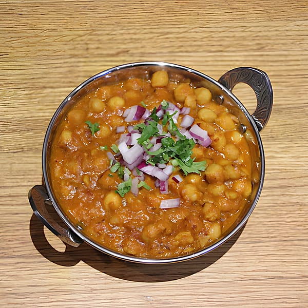 Mint Masala's chana masala, a chickpea curry, garnished with red onions and cilantro in a metal bowl.