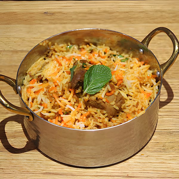 Mint Masala's Indian biryani with meat and rice, garnished with a mint leaf, in a brass pot.