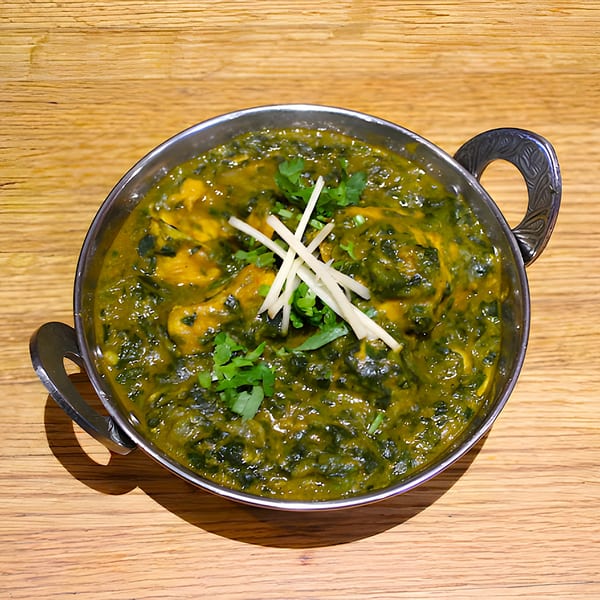 A metal bowl of vibrant green Indian palak paneer, garnished with fresh cilantro and ginger slivers.