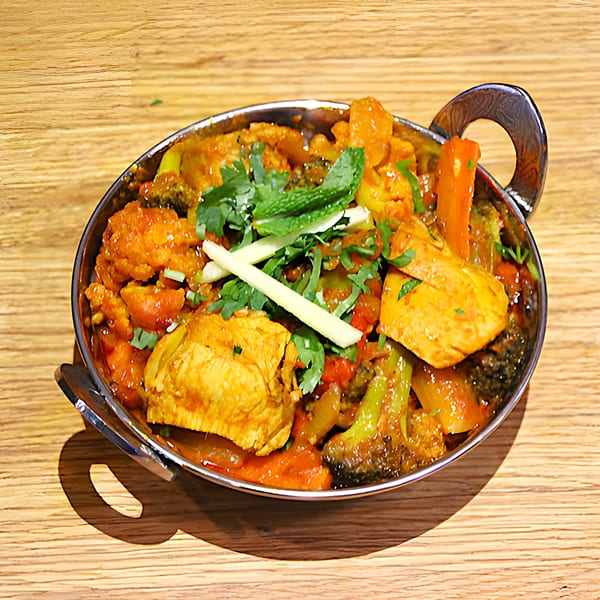 Mint Masala's Indian curry with chicken, vegetables, and herbs in a metal bowl on a wooden table.