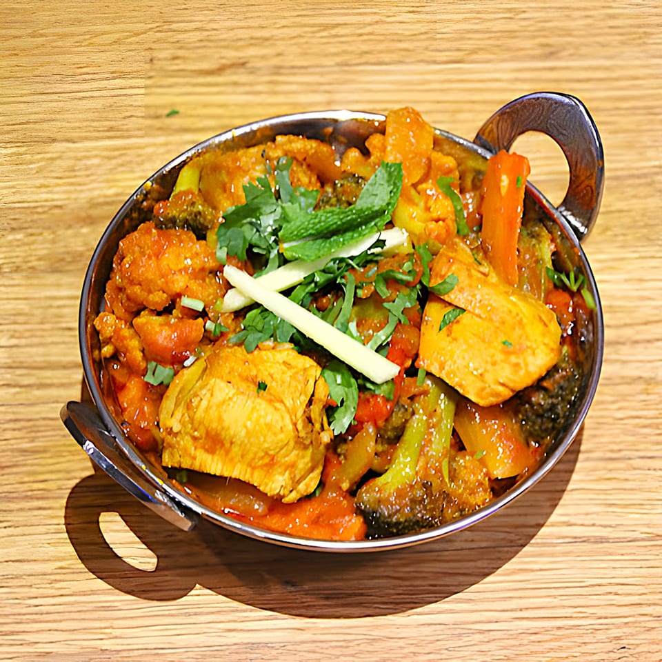 Mint Masala's Indian curry with chicken, vegetables, and herbs in a metal bowl on a wooden table.